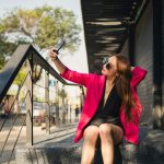 a woman in a pink jacket and black dress sitting on a set of stairs