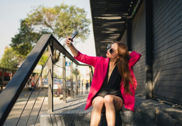 a woman in a pink jacket and black dress sitting on a set of stairs